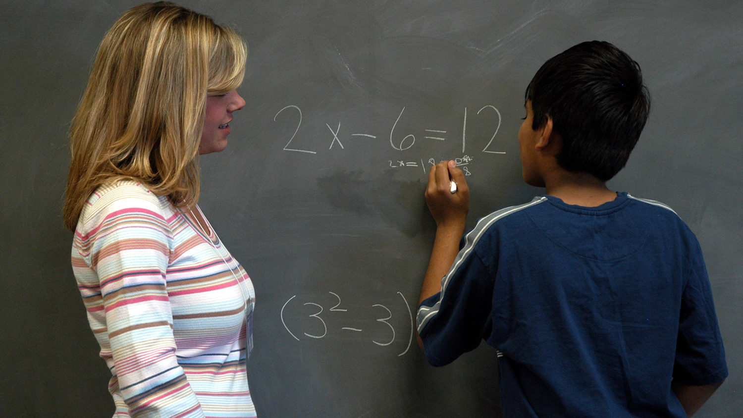 teacher working with student at chalkboard